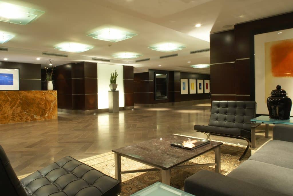 Elegant residential lobby featuring a marble reception desk, curated art, and classic leather seating, showcasing the premium design standards of The Benvenuto Group apartments.