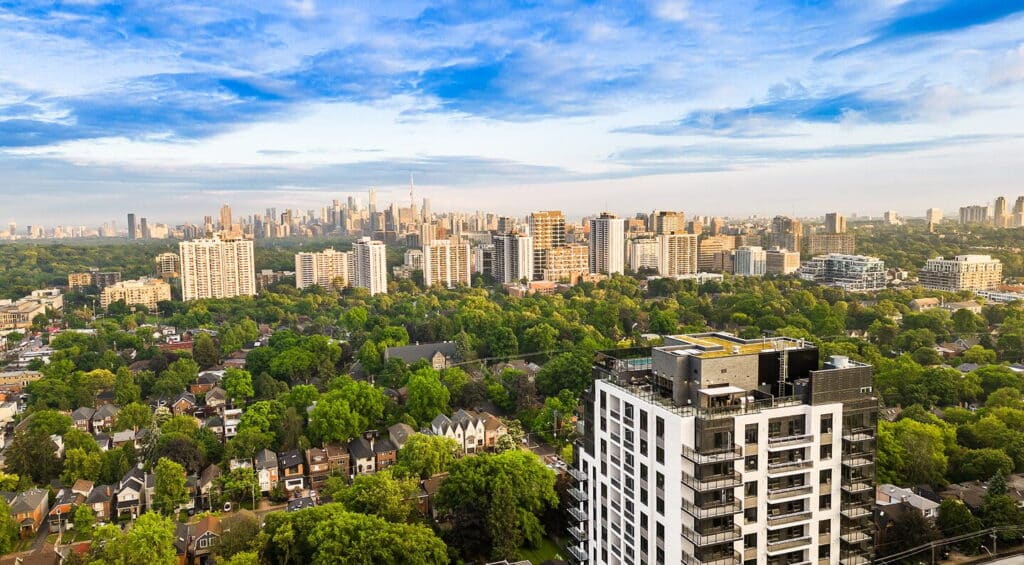 Aerial view of The Whitney on Redpath luxury apartment building near Yonge and Eglinton, surrounded by tree canopy with the downtown Toronto skyline.