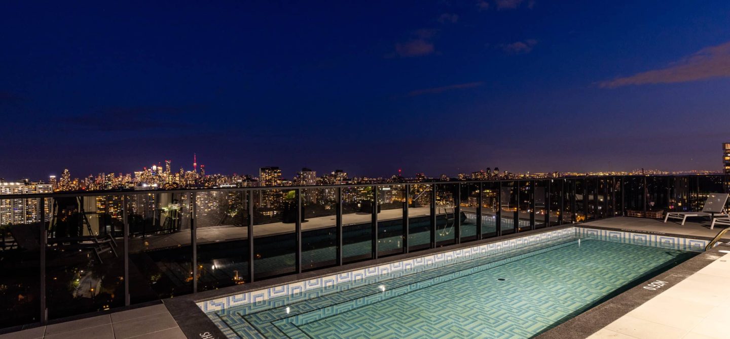 Exclusive rooftop swimming pool illuminated at night, featuring a spectacular view of the downtown Toronto skyline at our boutique luxury apartments.